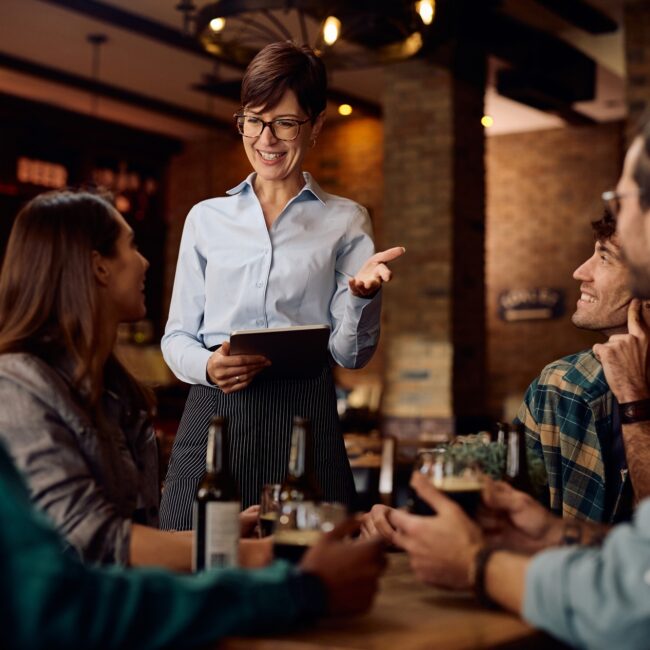 Happy waitress talking to group of guests in a bar.